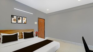 A neatly made bed with a dark brown bedspread, a wooden headboard, and black and white pillows. There are three framed artworks on the wall above the bed, and a wooden door to the right. - Super Townhouse Cherlapally Bus Terminal (Hyderabad)