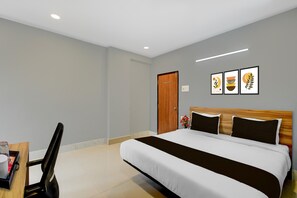 Een hotelkamer met een bed, een houten hoofdeinde, een bureau met stoel en een deur.