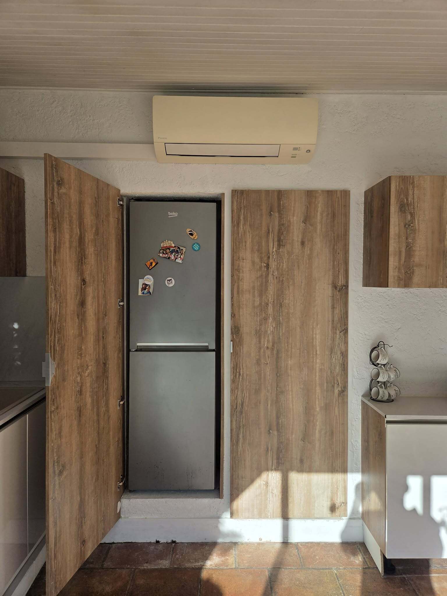 A kitchen with wooden paneling, a double-door refrigerator, and a wall-mounted air conditioner.