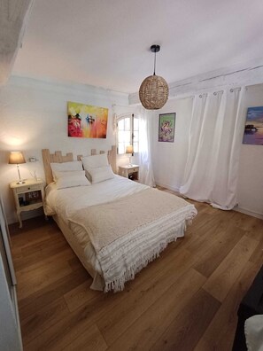 A bedroom with a wooden floor, a bed with white bedding, a hanging light fixture, and a painting on the wall. - Charming riverside house with pool and private riverbank (Tourrettes-sur-Loup)