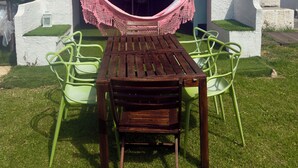 Une terrasse avec une table et des chaises en bois, un hamac et un mur blanc avec une fenêtre.