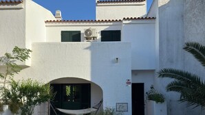 Un bâtiment blanc avec un toit recouvert de tuiles, un petit portail en arc de cercle et un chemin pavé menant à la porte.