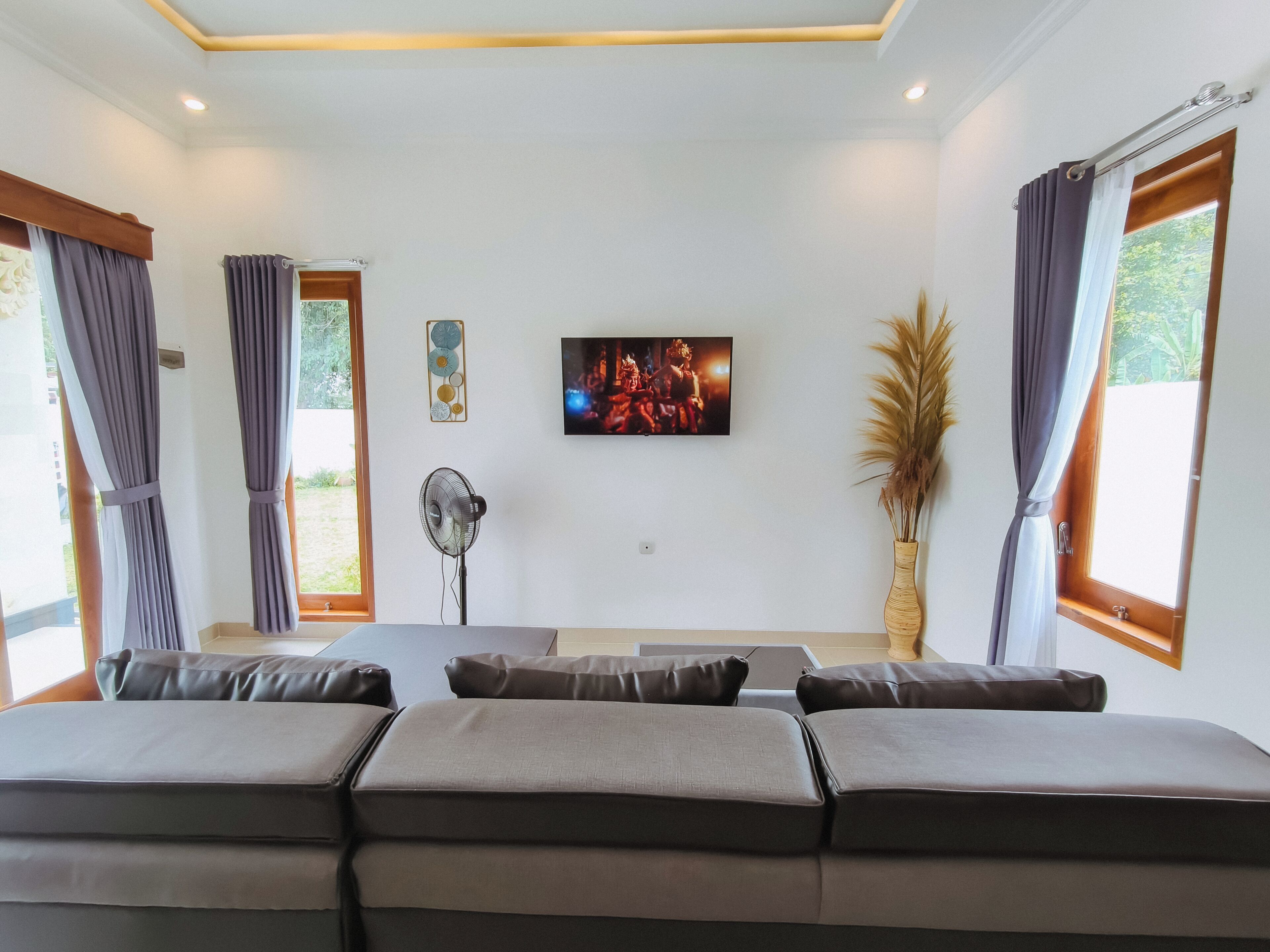 Un salon moderne avec un canapé, un téléviseur à écran plat, un ventilateur et une fenêtre avec des rideaux.