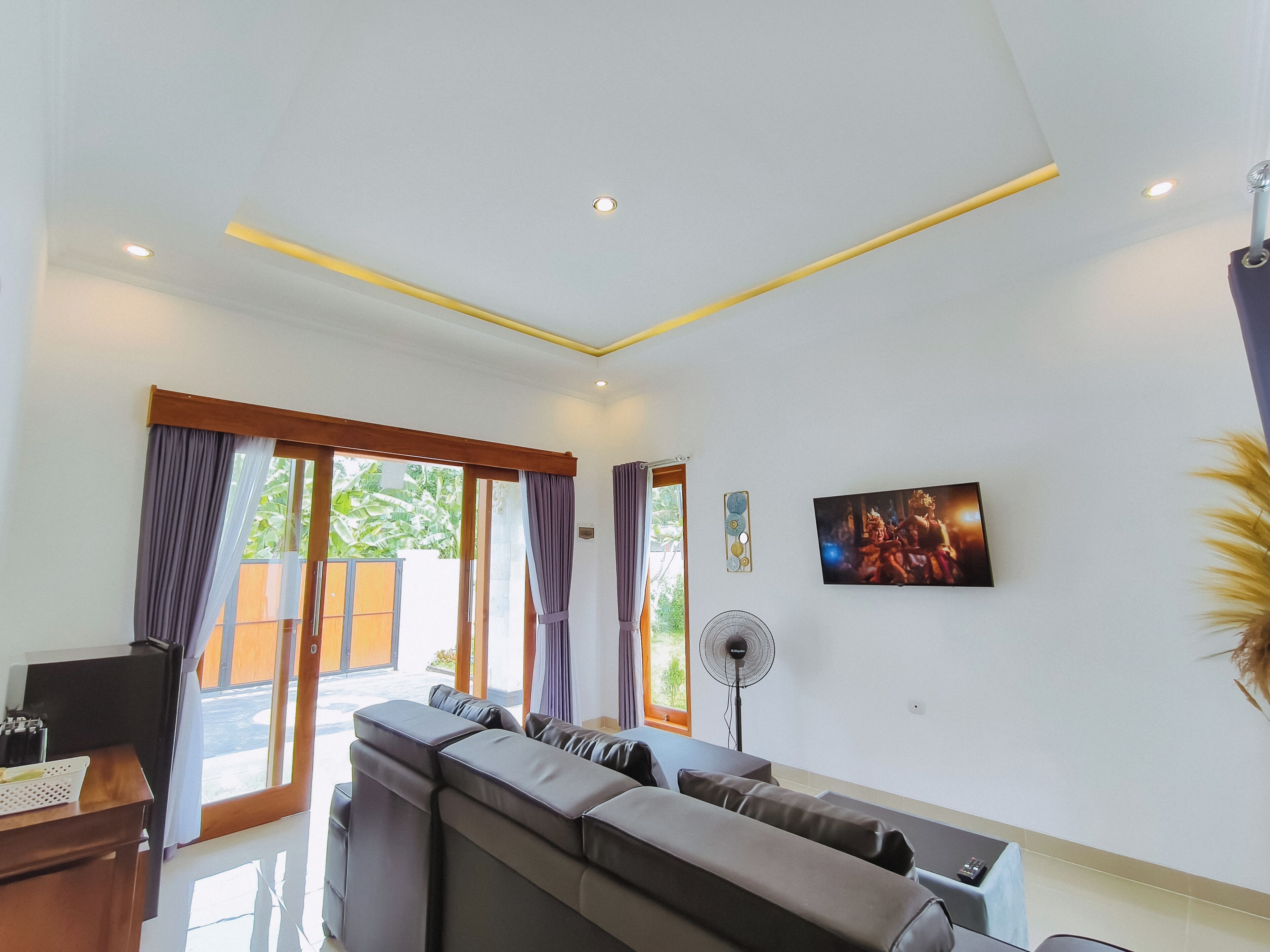 A modern living room with a sectional sofa, a flat-screen TV, and a fan.