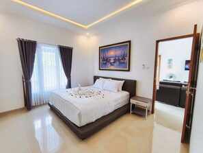 A hotel room with a bed, a nightstand, a desk, a chair, a painting, and a mirror. - Bali Lovina Karuna Villa near beach (Kabupaten Buleleng)