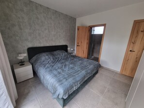 Un dormitorio con cama, mesita de noche, armario y puerta corrediza de vidrio.