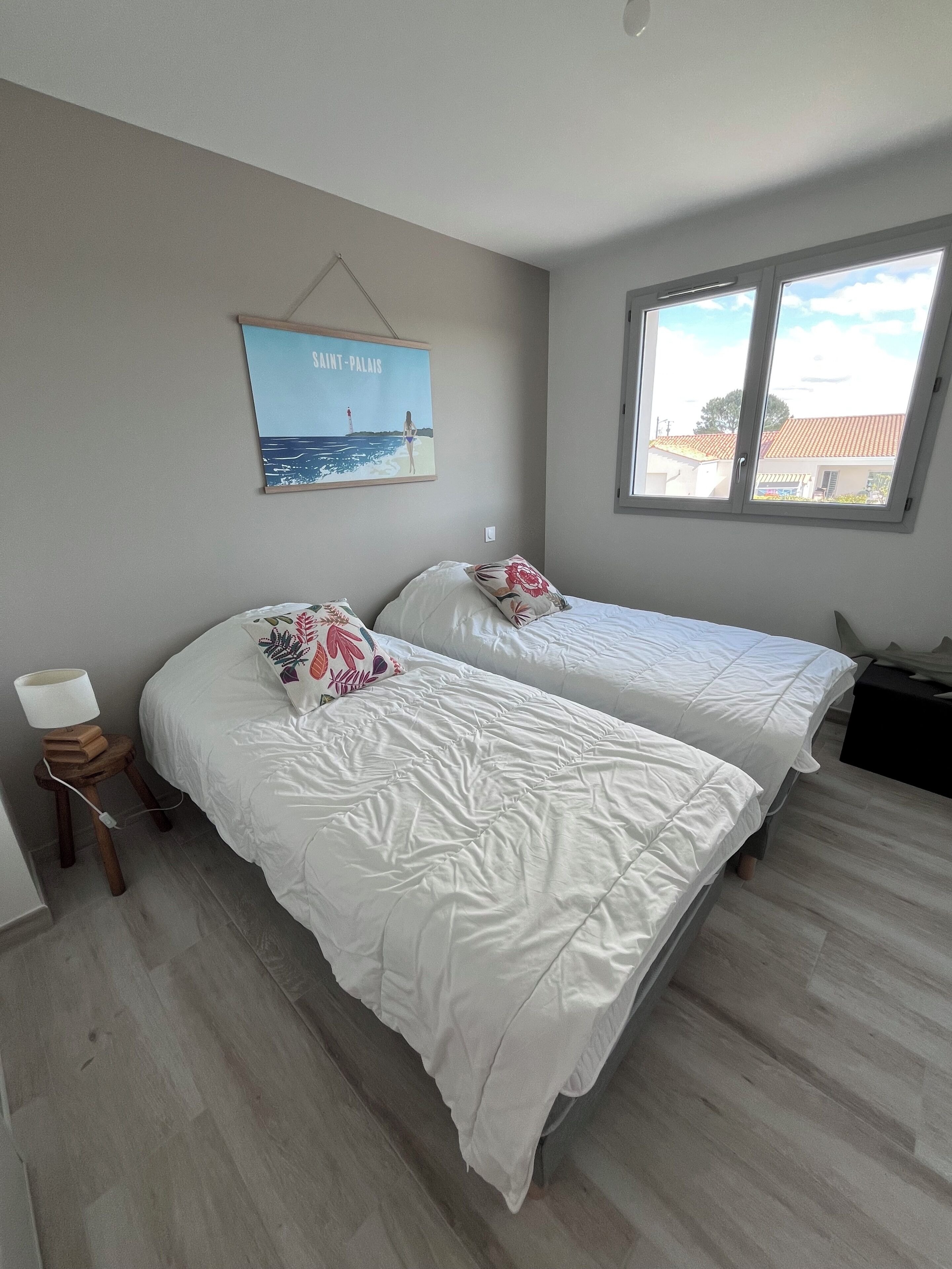 A bedroom with two beds, a nightstand, a lamp, a poster, and a window with a view.