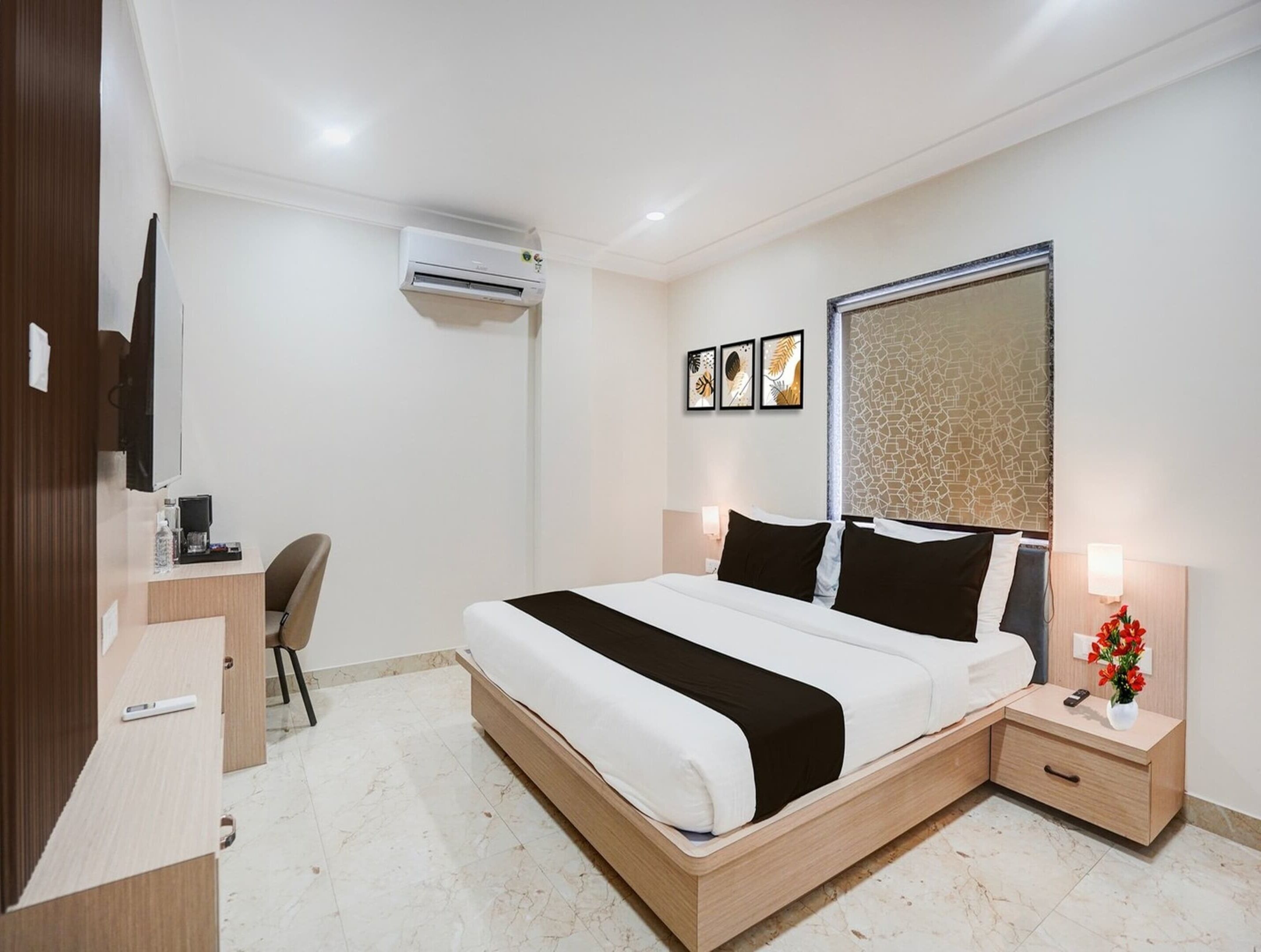 A modern hotel room with a bed, bedside tables, a desk, an air conditioning unit, and a wall-mounted TV.