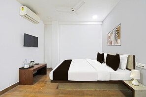 Ein Hotelzimmer mit Bett, Schreibtisch, Fernseher, Klimaanlage, Deckenventilator und Kunstwerken an der Wand.