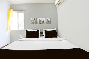 Ein Hotelzimmer mit einem Bett, einem Fenster mit Vorhängen und drei an der Wand befestigten Kunstwerken.