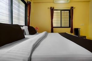 Ein Hotelzimmer mit einem Bett, einem kleinen Tisch, einem Sessel, einem Fenster mit Vorhängen und einer Wandklimaanlage.