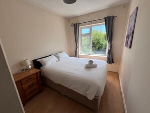 A bedroom with a bed, a nightstand, a window with curtains, and a wall-mounted picture.