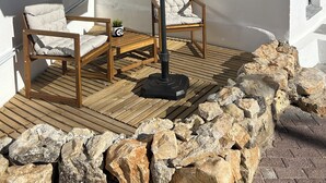 A patio with two chairs, an umbrella, and a wooden deck. - Modern Studio with Private Patio near Cascais and Sintra (Alcabideche)