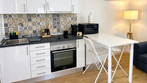 A compact kitchen with white cabinets, a patterned backsplash, a microwave, an oven, and a foldable dining table. - Modern Studio with Private Patio near Cascais and Sintra (Alcabideche)