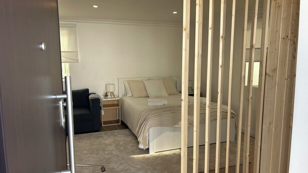 A bedroom with a bed, bedside table, lamp, and a wooden partition. - Modern Studio with Private Patio near Cascais and Sintra (Alcabideche)