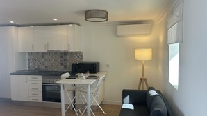 A compact living space with a kitchenette, a dining area, a sofa, and a floor lamp. - Modern Studio with Private Patio near Cascais and Sintra (Alcabideche)