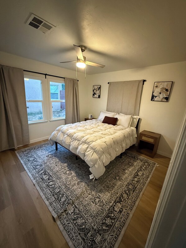 A bedroom with a bed, a ceiling fan, a window, and a nightstand.