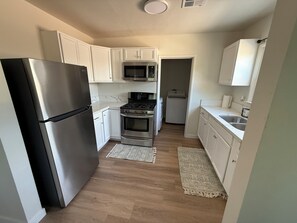 A compact kitchen with white cabinets, stainless steel appliances, and a wooden floor.