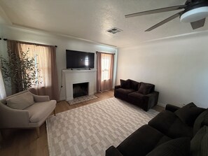 A living room with a fireplace, a television, a ceiling fan, and two sofas.