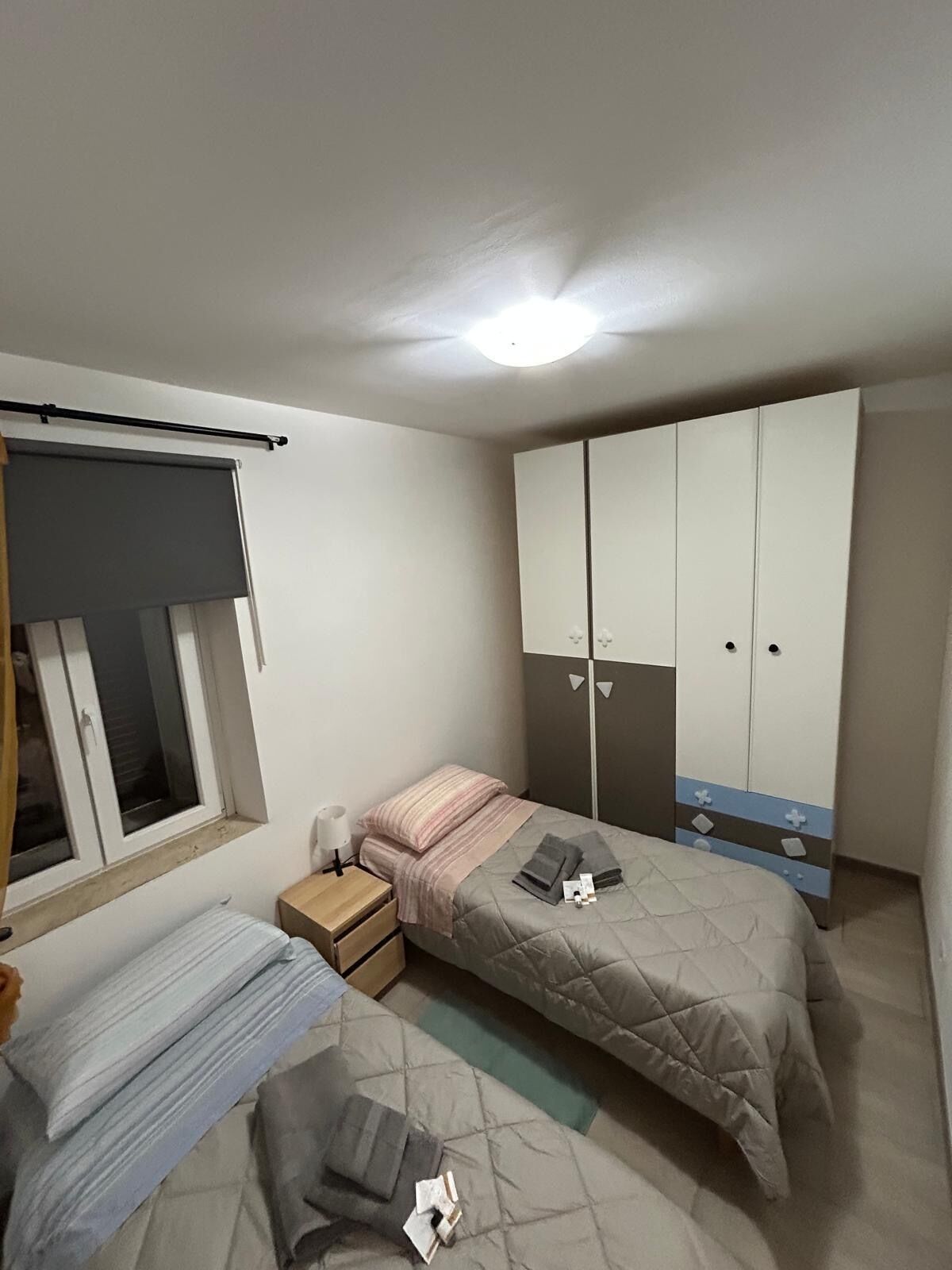A bedroom with a bed, a wardrobe, a bedside table, and a window.