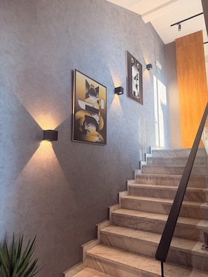 A staircase with a modern design, a wall with two framed artworks, and a potted plant. - XIO Apartments (Bar)