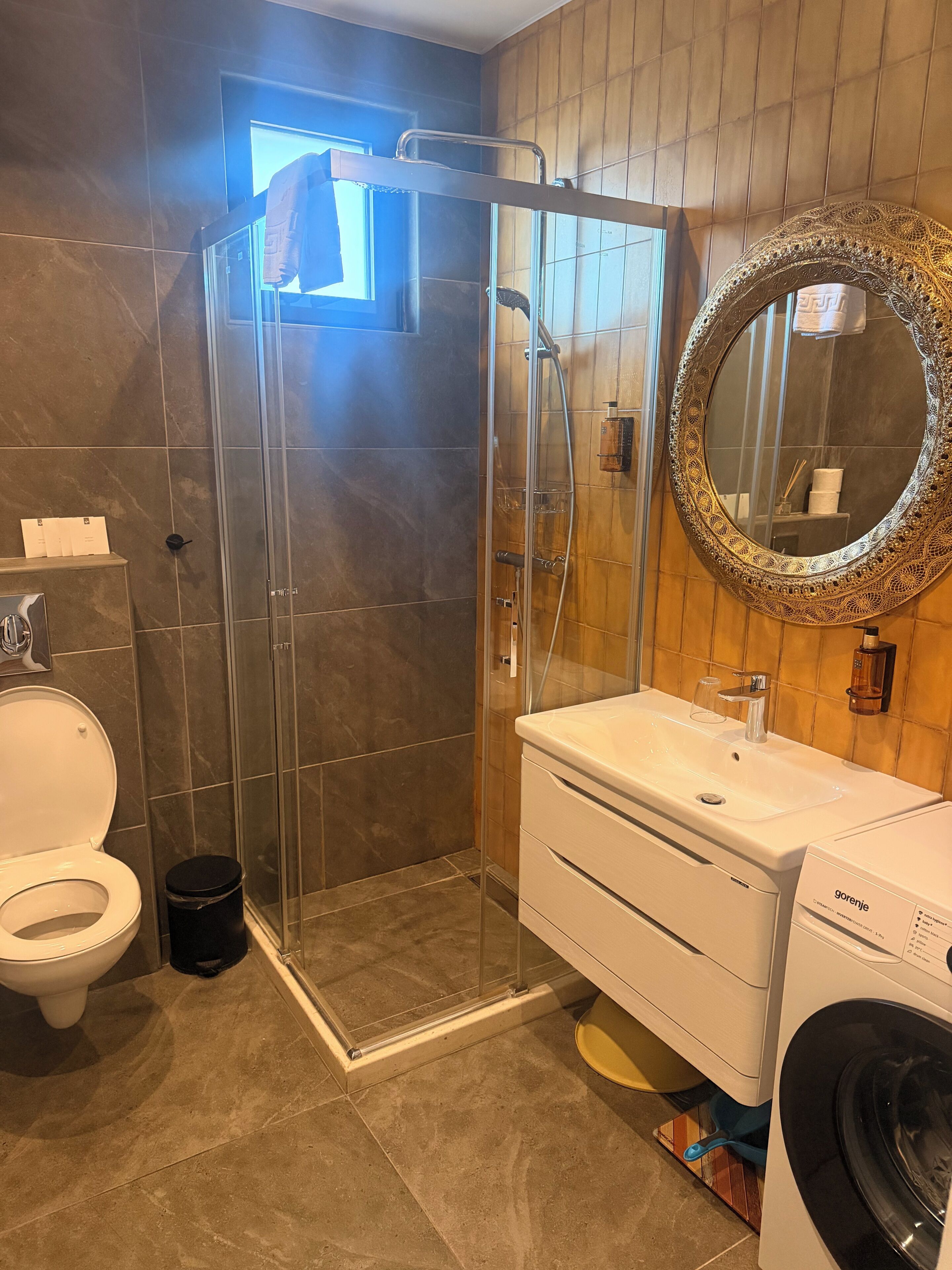 Ein Badezimmer mit Duschkabine, Waschbecken mit Spiegel, Toilette und Waschmaschine.
