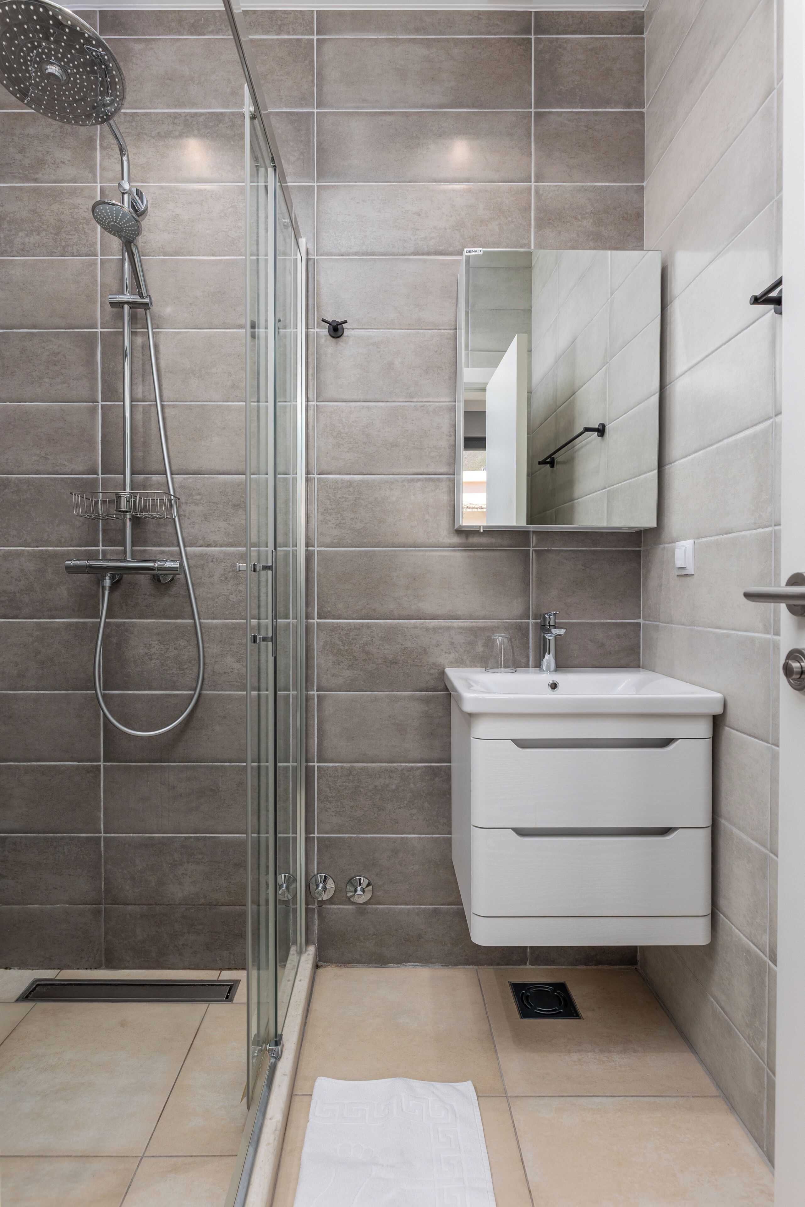 Un baño moderno con cabina de ducha de vidrio, lavabo blanco y espejo.