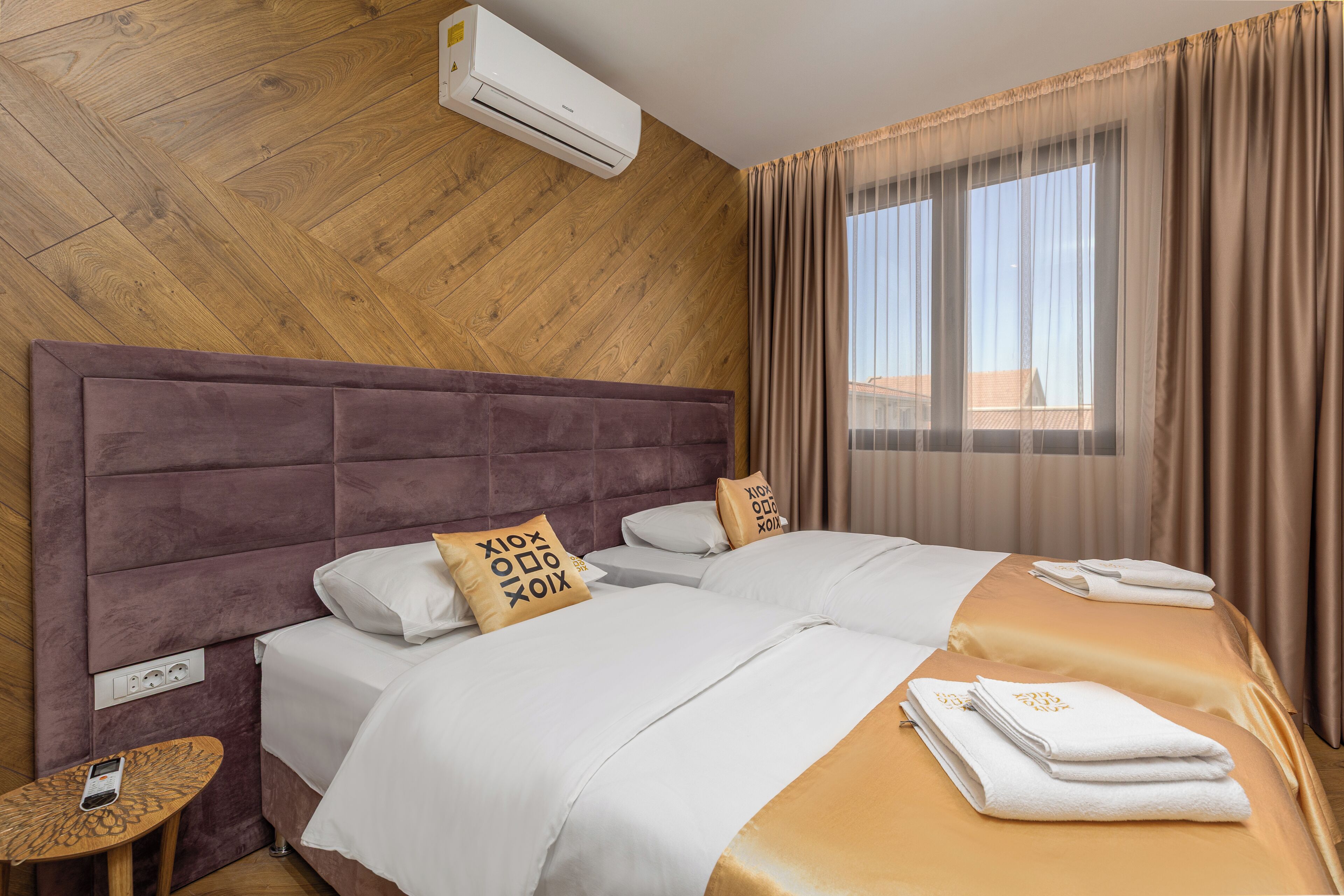 Habitación de hotel con pared de madera, una cama grande con ropa blanca, una mesita con teléfono y una ventana con cortinas.