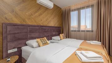Habitación de hotel con pared de madera, una cama grande con ropa blanca, una mesita con teléfono y una ventana con cortinas.