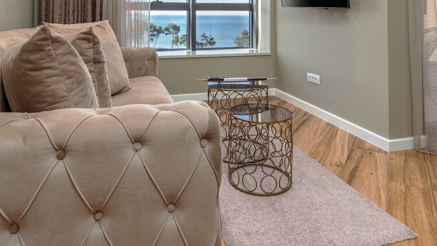 A living room with a sofa, a TV mounted on the wall, a window with a view, and a small table with a lamp. - XIO Apartments (Bar)
