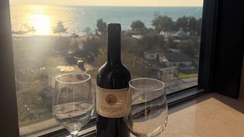A wine bottle and two glasses on a table by a window with a view of the ocean.