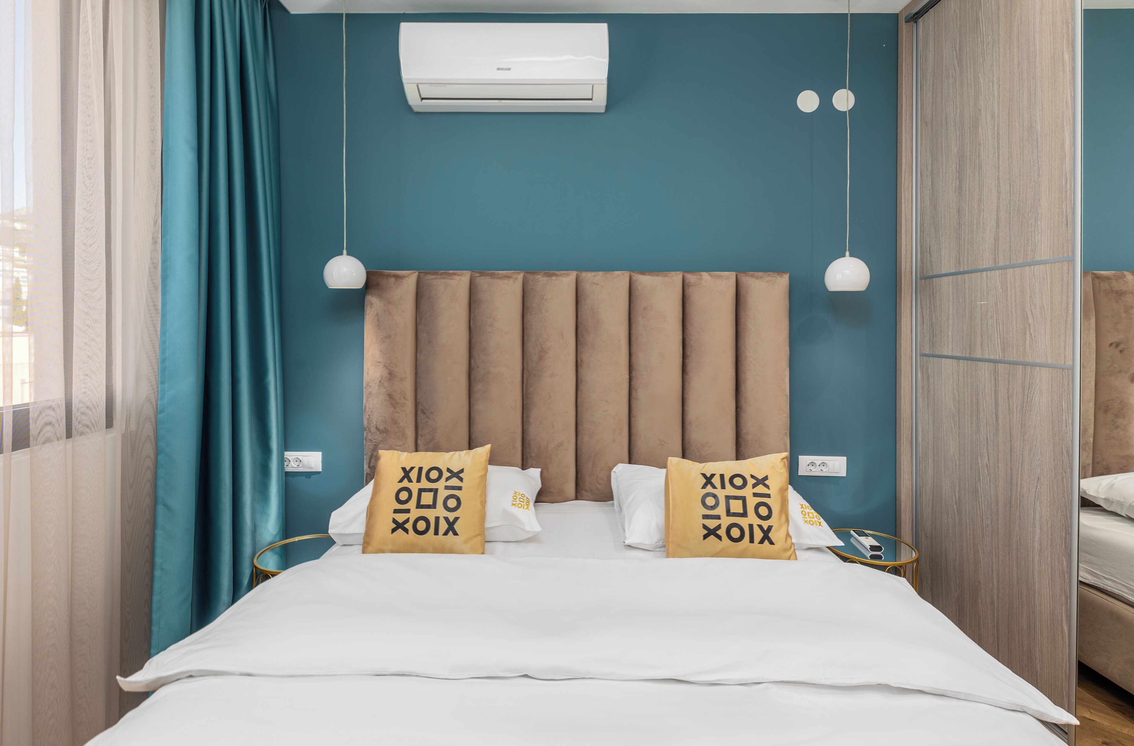 A bedroom with a bed, two bedside lamps, an air conditioning unit, and a window with curtains.