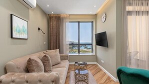 A living room with a sofa, a coffee table, a TV, and a large window with a view. - XIO Apartments (Bar)