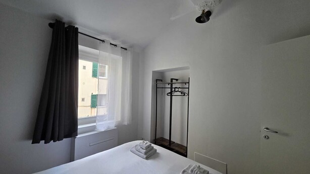 Una habitación de hotel con cama, ventana con cortinas, perchero y puerta.