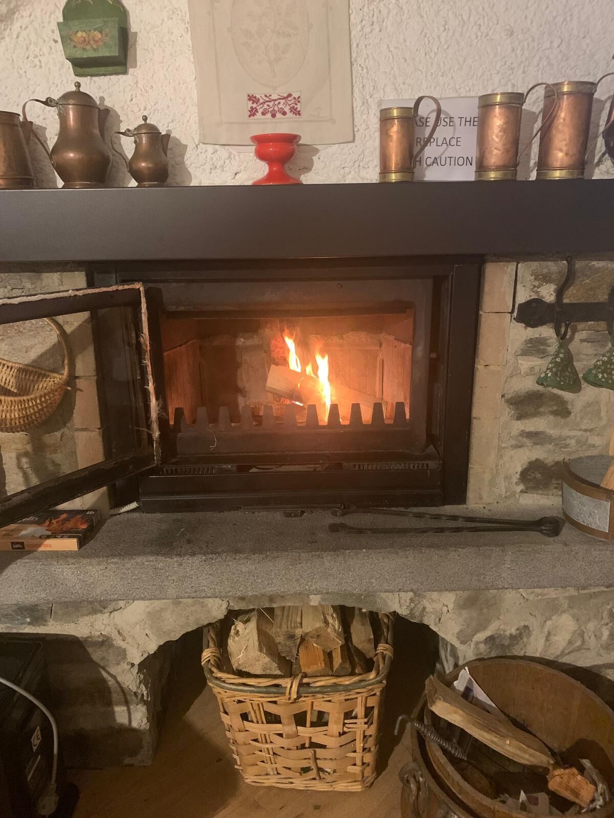 Un camino con un fuoco acceso, un cesto di legna e un cartello sopra il camino.