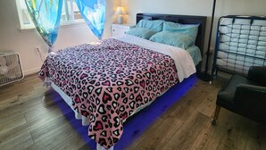 Ein Schlafzimmer mit einem Bett, einem Nachttisch, einer Lampe, einem Sessel und einem Fenster mit Vorhängen.