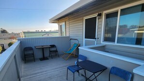 Eine Holzterrasse mit Tisch und Stühlen, einem blauen Liegestuhl und einem Fenster mit Blick auf ein Gebäude.
