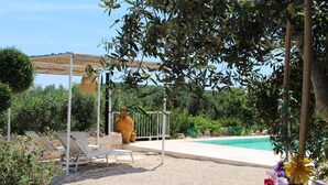 A pool area with lounge chairs, a pergola, and a decorative flower arrangement. - Cozy medieval trullo for couples and families seeking tranquility. (OSTUNI)