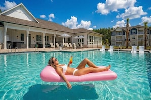 Un espace piscine avec des chaises longues, un bâtiment doté d’un patio couvert et un ciel d’un bleu éclatant.