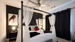 A four-poster bed with white bedding, a black headboard, and a canopy. There is a nightstand with a lamp and a framed picture on the wall. - Family Cinema Escape · Salt Pool · Gym · Sleeps 8 (Yulee)
