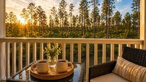 A balcony with a wicker table, two cups of coffee, and a view of a forest. - Family Cinema Escape · Salt Pool · Gym · Sleeps 8 (Yulee)
