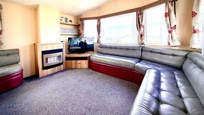 Una sala de estar acogedora con sofá, televisión, estantería y ventana con cortinas.