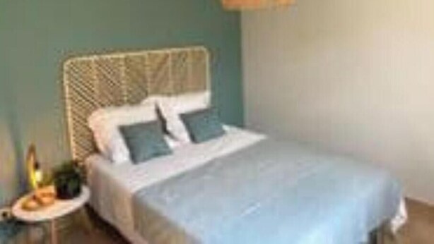 A bed with a white headboard and blue bedding, a small bedside table with a lamp, and a hanging light fixture. - Villa with swimming pool and garrigue view near Montpellier - calm and comfort (Pignan)