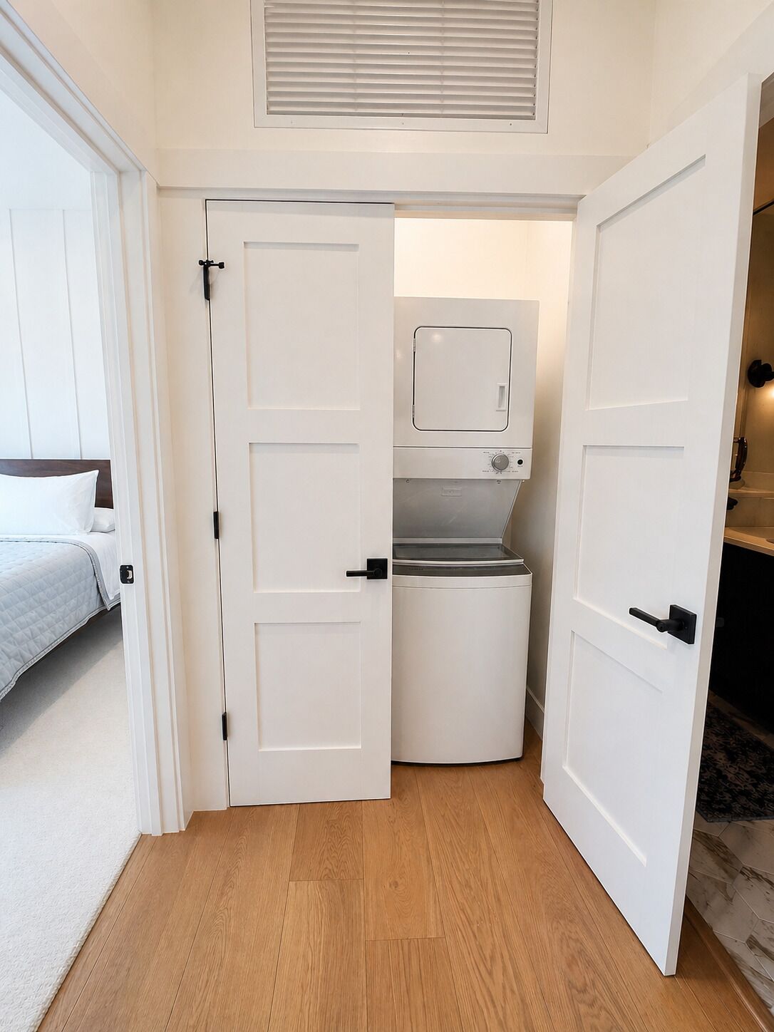 A compact room with a bed, a washing machine, and a door leading to another room.