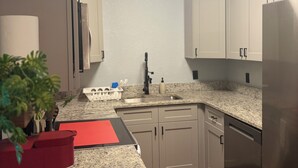 A compact kitchen with white cabinets, a stainless steel refrigerator, a granite countertop, and a potted plant. - Amelias Arena Retreat 4bedroom home in Orlando (Orlando)
