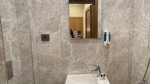 A bathroom with a marble wall, a sink, a mirror, and a toilet. - Otel Bergama (İstanbul)