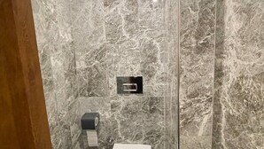 A bathroom with a marble wall, a toilet, a paper towel dispenser, and a flush handle. - Otel Bergama (İstanbul)