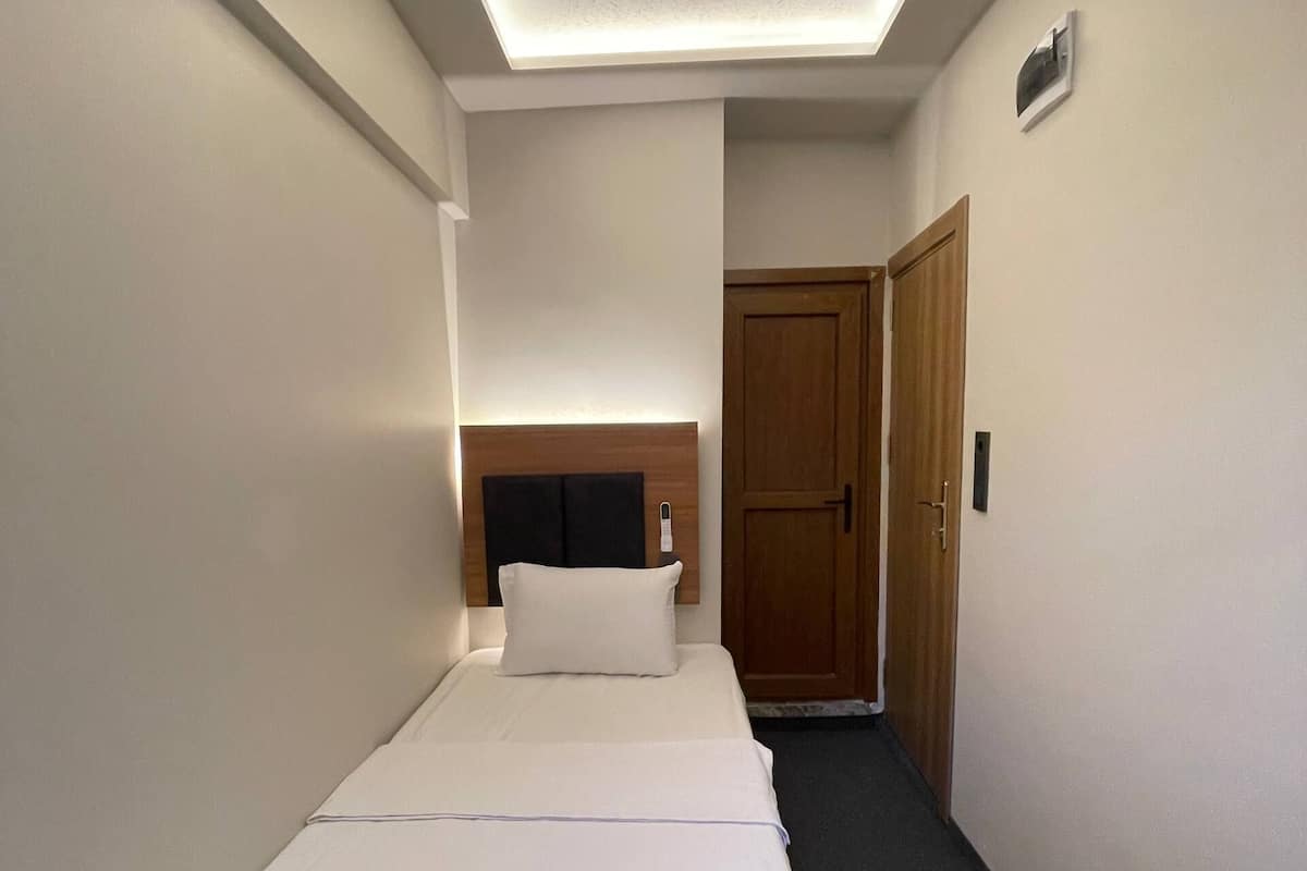 A single bed with a headboard, a bedside table, a wooden door, and a small wall-mounted light fixture.