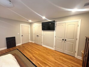 A room with hardwood flooring, white doors, a mounted TV, and a bed with a white comforter.