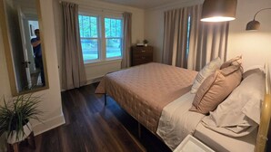 Une chambre à coucher comprenant un lit, un ventilateur de plafond, une lampe de chevet, une commode et une fenêtre avec des rideaux.